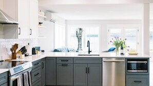 A modern kitchen with grey cabinets, a stainless steel dishwasher, and a built-in oven. - Luxury Roxbury Pond Lakefront (Roxbury)