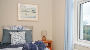 A bedroom with a bed, pillows, a bedside table with a lamp, and a window. - 4 Polgrain Turning (Bodmin)