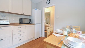 A modern kitchen with white cabinets, a microwave, and a dining area with a table set for breakfast. - 4 Polgrain Turning (Bodmin)