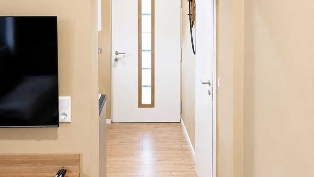 Passadís amb un televisor fixat a la paret, una estant de fusta amb un comandament i una porta amb un portaTovalloles.