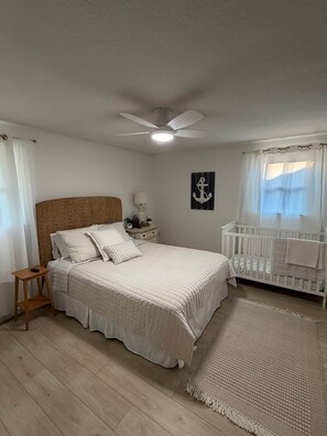 A bedroom with a bed, a crib, a ceiling fan, a nightstand, and a wall-mounted lamp. - The Abiding Place - Clear Lake (Cerro Gordo County)