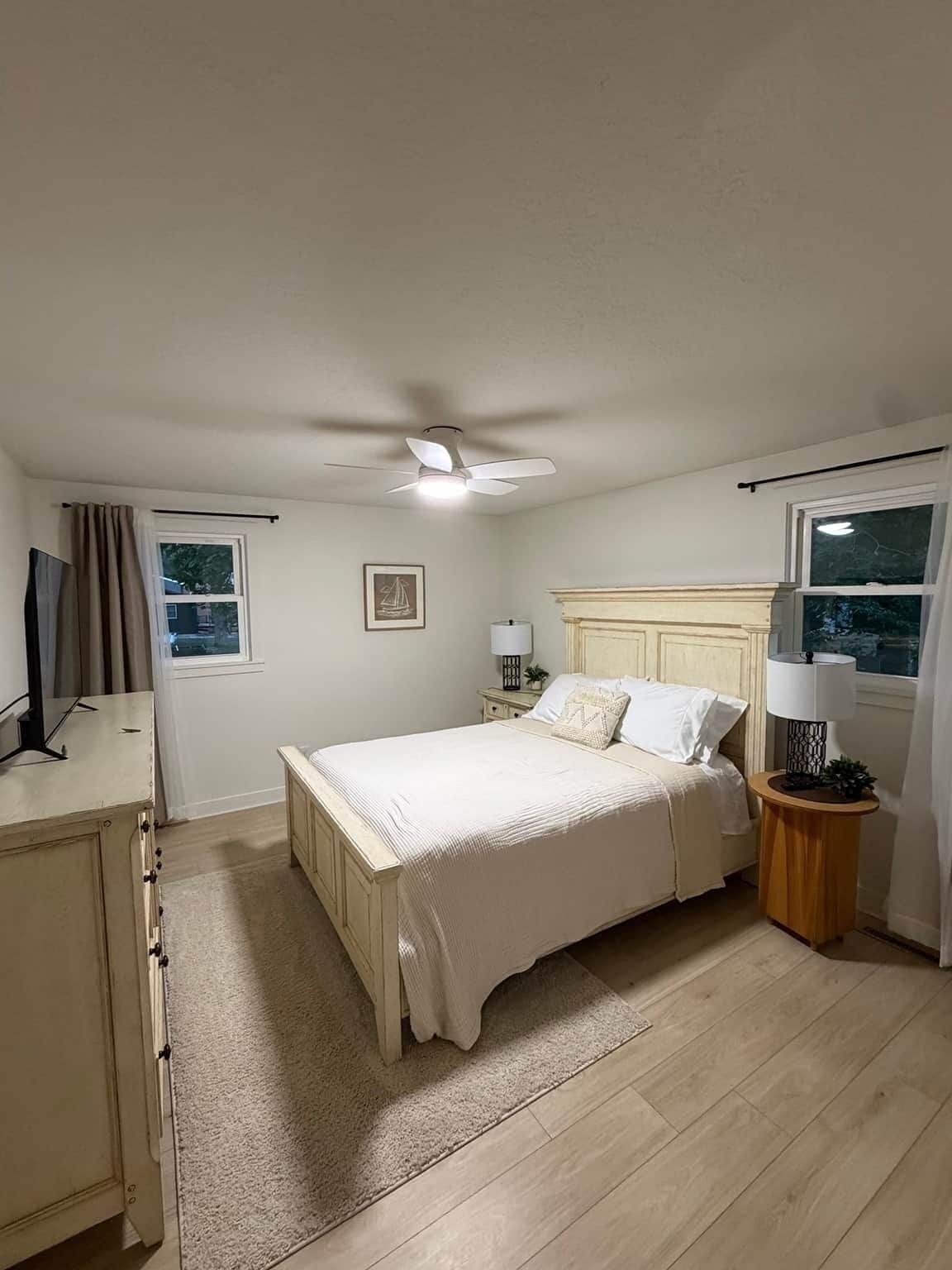 Une chambre à coucher avec un lit, des tables de chevet, un ventilateur de plafond et une fenêtre.