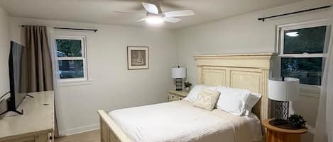 Une chambre à coucher avec un lit, des tables de chevet, un ventilateur de plafond et une fenêtre.