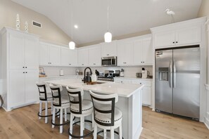 Uma cozinha moderna com armários brancos, geladeira de aço inoxidável e uma ilha central com banquetas.