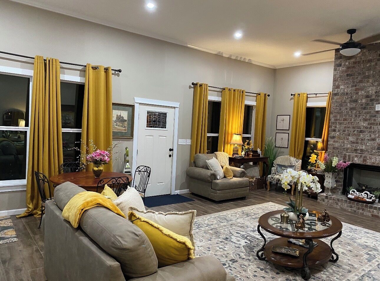 Een woonkamer met een bank, fauteuils, een salontafel en gele gordijnen.