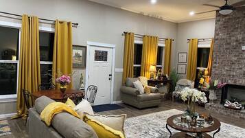 Een woonkamer met een bank, fauteuils, een salontafel en gele gordijnen.
