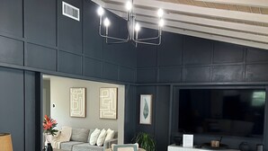 A modern living room with a sofa, chairs, a coffee table, a TV, and a ceiling with exposed beams. - Modern house with pool near Downtown (Lakeland)