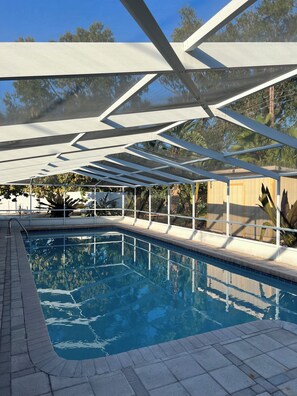 En swimmingpool med krystalklart, blåt vand, omgivet af et overdækket område med en geometrisk konstruktion i metal.