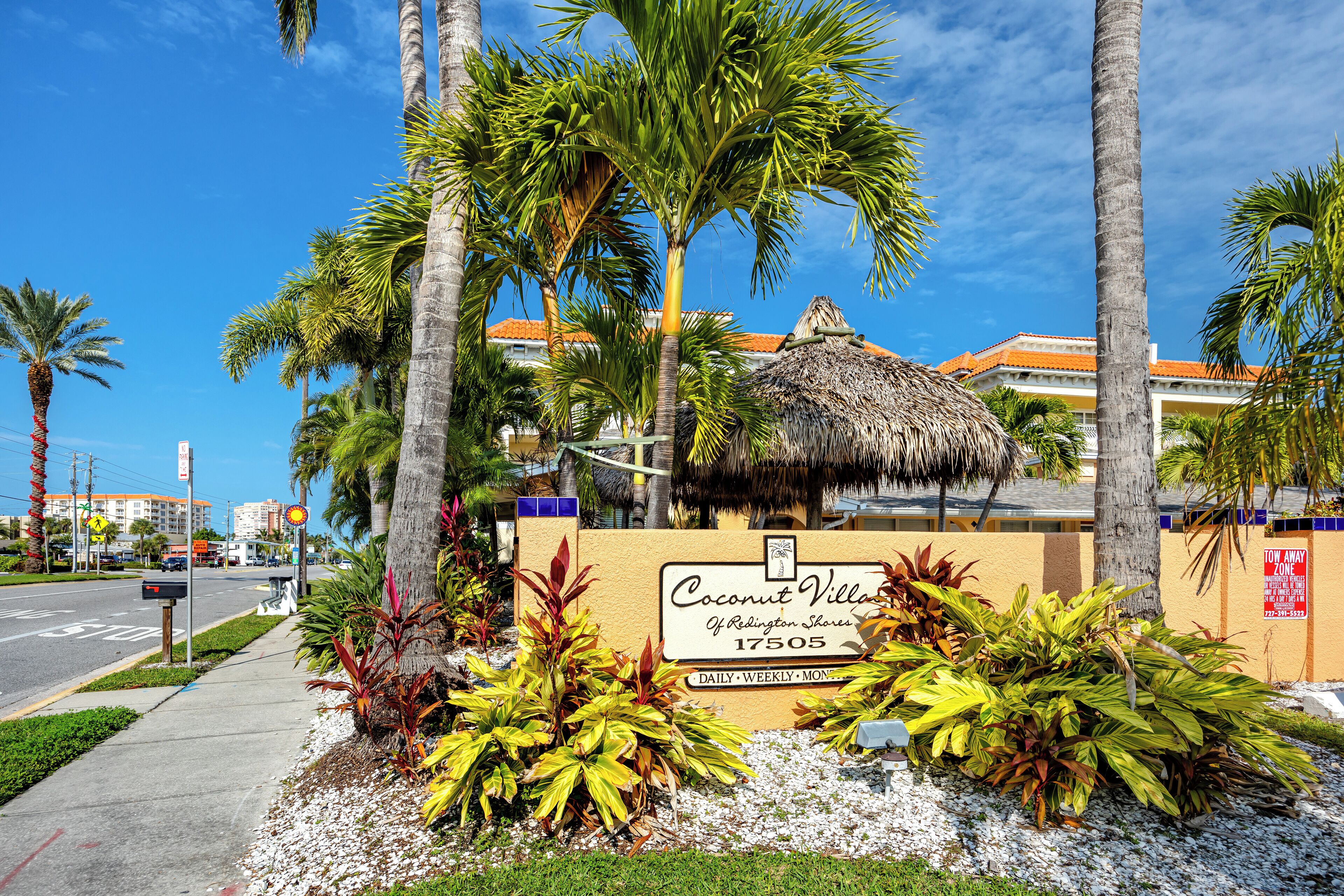 Une enseigne pour le complexe Coconut Village de Ridlington Shores, représentant un jardin tropical avec des palmiers et une structure à toit de chaume.