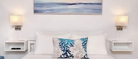 A hotel room with a bed, white bedding, a painting of a landscape, and two bedside tables with lamps.