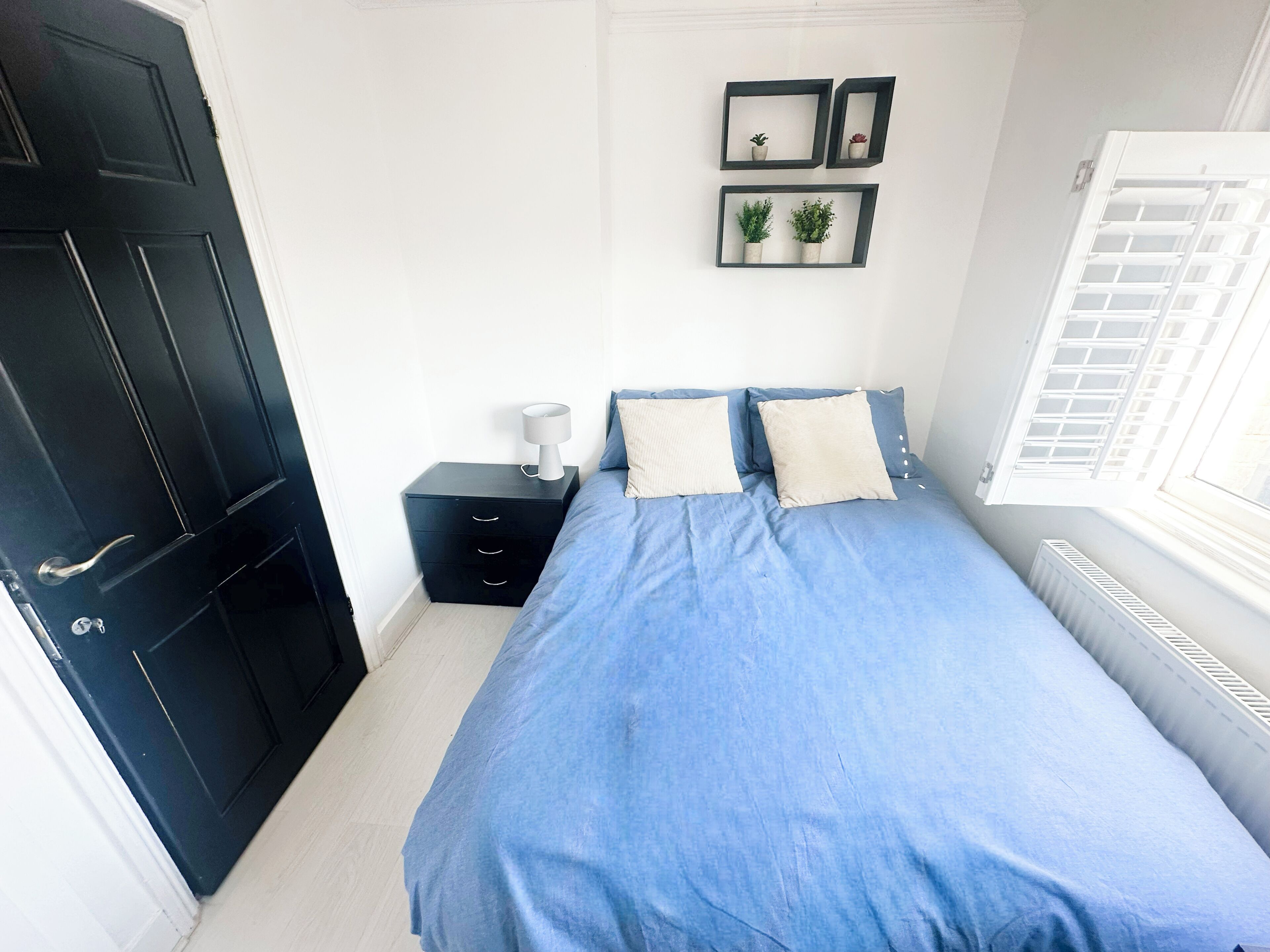 A bedroom with a bed, a nightstand, a dresser, a door, and a window with blinds.