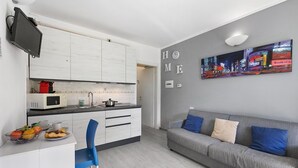 A modern kitchen with white cabinets, a microwave, and a dining area with a blue chair. - Mobilehome in Porlezza am Luganersee (Porlezza)