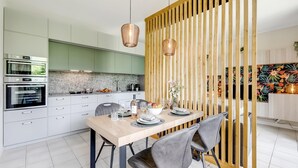 A modern kitchen with white cabinets, a built-in oven, and a dining area with a wooden partition. - Mobilehome in Porlezza am Luganersee (Porlezza)