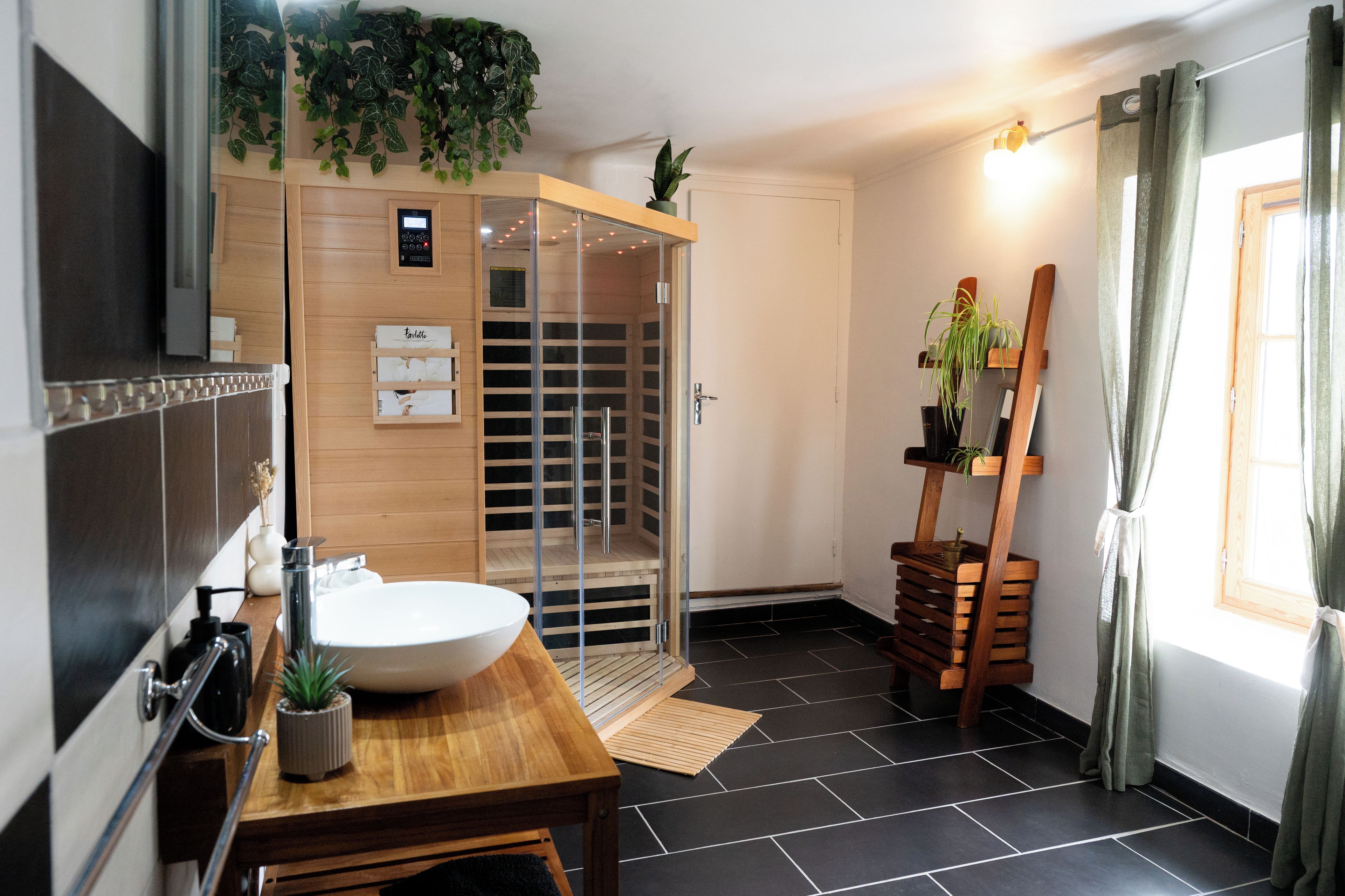 A modern bathroom with a wooden vanity, a large sink, a glass-enclosed shower, and a wooden shelf with plants.