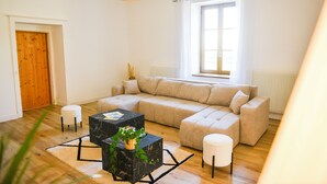 Una sala moderna con un sofá seccional, una mesita de centro de mármol, un otoman pequeño y redondo, y una lámpara colgante.