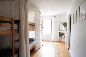 A room with bunk beds, a window with curtains, a bookshelf, and a mirror on the wall. - Gîte du soleil levant (Menétru-le-Vignoble)