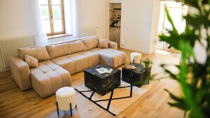 A living room with a sectional sofa, two black marble coffee tables, a white ottoman, and a wooden floor.