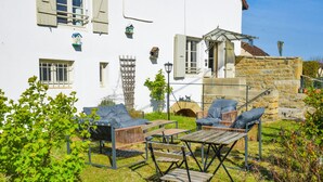 A white building with a stone wall, outdoor seating with cushions, and a small garden area.