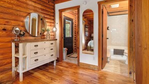 Interno di una baita di legno, con un comò, uno specchio e una porta che dà su un bagno.