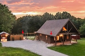 A log cabin with a porch, a small shed, and a covered area with string lights.