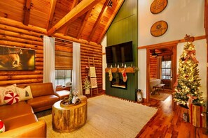A cozy log cabin interior with a fireplace, a Christmas tree, and a comfortable seating area.