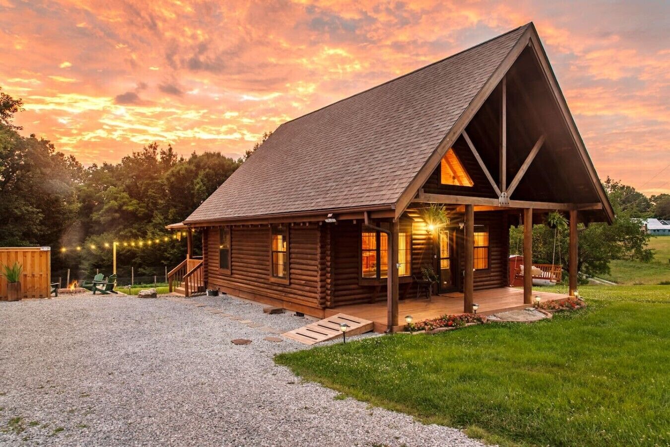 A log cabin with a porch, a fire pit, and string lights.