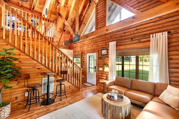 A log cabin interior with a staircase, a sofa, a coffee table, and a dining area.