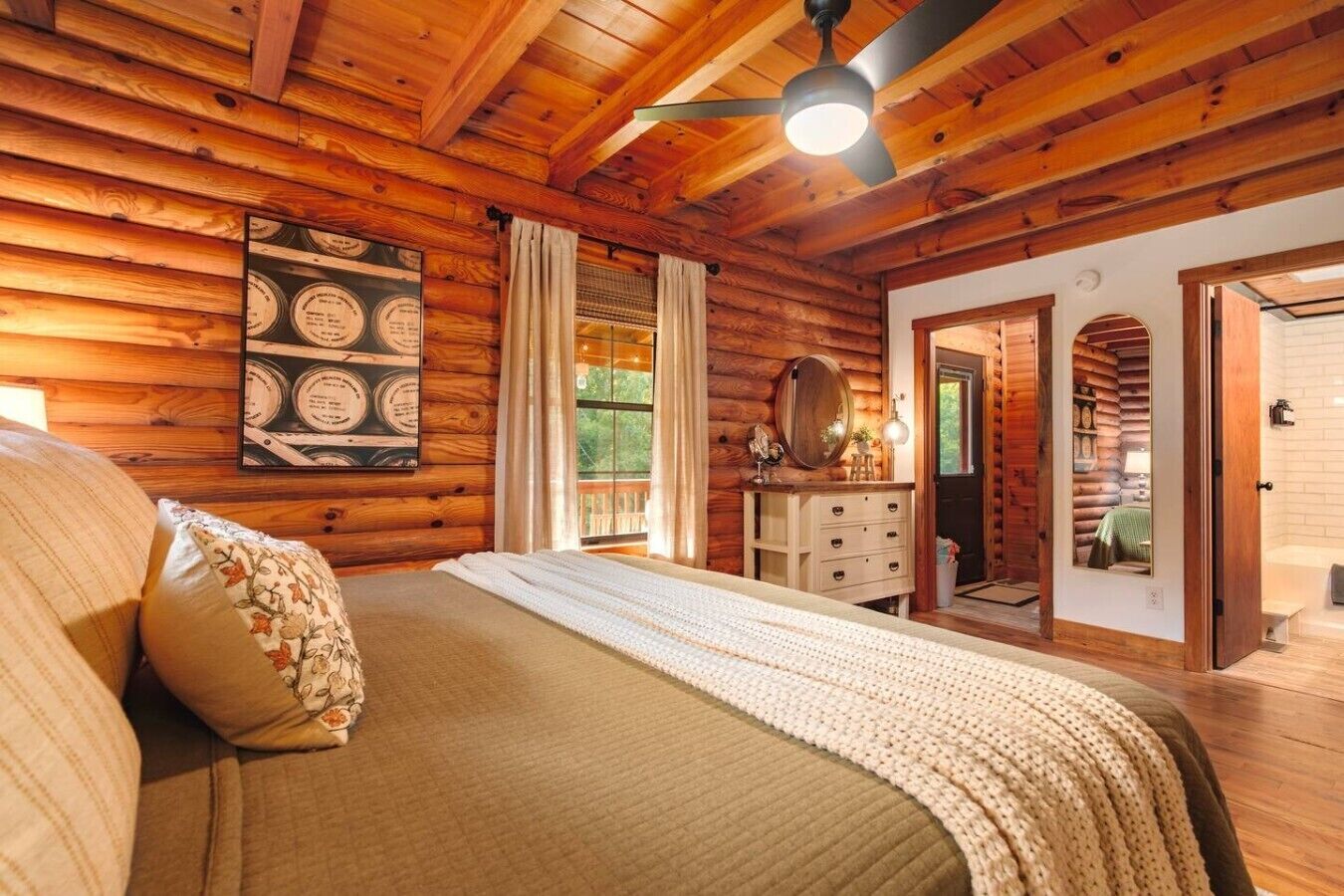 A log cabin bedroom with a bed, a dresser, a mirror, and a ceiling fan.