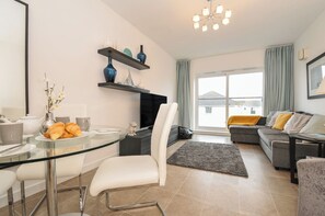 A modern living room with a glass dining table, white chairs, a sofa, and a TV. - Sea Snug (Newquay)