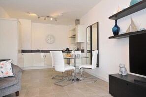 A modern kitchen with white cabinets, a dining table with two white chairs, and a clock on the wall. - Sea Snug (Newquay)
