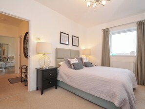 A bedroom with a bed, bedside lamps, a nightstand, a mirror, and a window with curtains. - Sea Snug (Newquay)