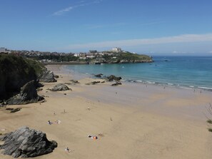 A beach with rocky areas, a clear sky, and buildings in the background. - Sea Snug (Newquay)