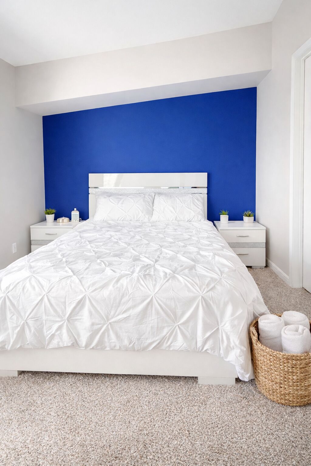 Un dormitorio con cama blanca, pared azul decorativa y una mesita de noche con una planta.