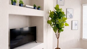 A living room with a flat-screen TV on a white shelf, a potted plant, and framed artwork on the wall. - 5-STAR Sarasota Stay Luxur 2BR/2BA (Sarasota)