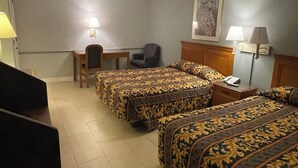 Ein Hotelzimmer mit zwei Betten, einem Schreibtisch, einem Stuhl und einem Nachttisch mit Lampe.