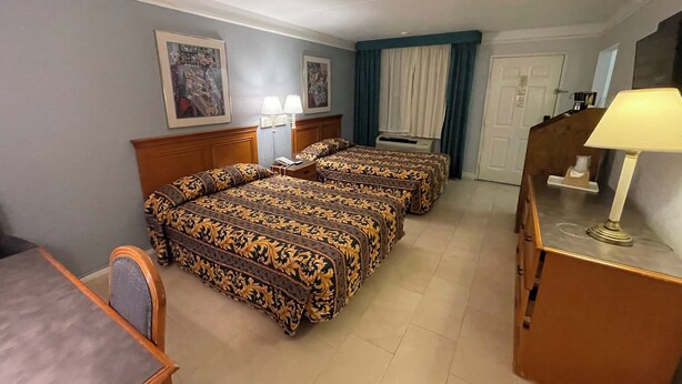 Ein Hotelzimmer mit zwei Betten, einem Schreibtisch, einem Stuhl, einer Lampe und einer Tür.