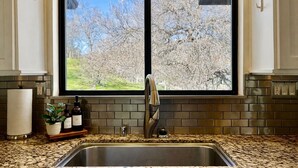 A kitchen with a double sink, a window with a view of trees, and a countertop with a plant and bottles. - 10 minutes to Sequoia Park Entrance/Hot Tub/Fire Pit/Pet Friendly/Mountain Views (Three Rivers)
