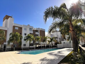 A modern apartment complex with a swimming pool, palm trees, and a clear blue sky. - Porto Caravelas (Florianópolis)