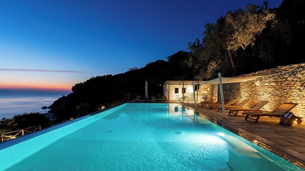 Une piscine à l’eau d’un bleu cristallin, entourée de murs en pierre et de chaises longues.