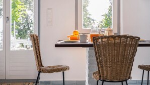 Un coin repas avec des chaises en osier, une table sur laquelle se trouve une carafe de jus d’orange, et une vue sur la verdure à l’extérieur.