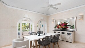 A dining area with a white table, four chairs, a ceiling fan, and a cabinet with a mirror and decorative items. - Royal Villa - Royal Westmoreland - Modern Tropical Villa (Saint James)
