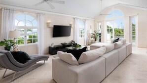 A spacious living room with a sofa, a coffee table, a TV, and large windows. - Royal Villa - Royal Westmoreland - Modern Tropical Villa (Saint James)
