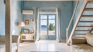 A room with a wooden staircase, a sofa, a cabinet with children's books, and a view of the sea through a glass door. - Laeticia - Seven Bedroom Villa, Sleeps 14 (Finikas)