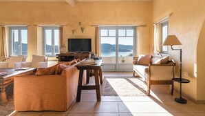 A living room with a TV, sofas, a coffee table, and a view of the sea. - Laeticia - Seven Bedroom Villa, Sleeps 14 (Finikas)