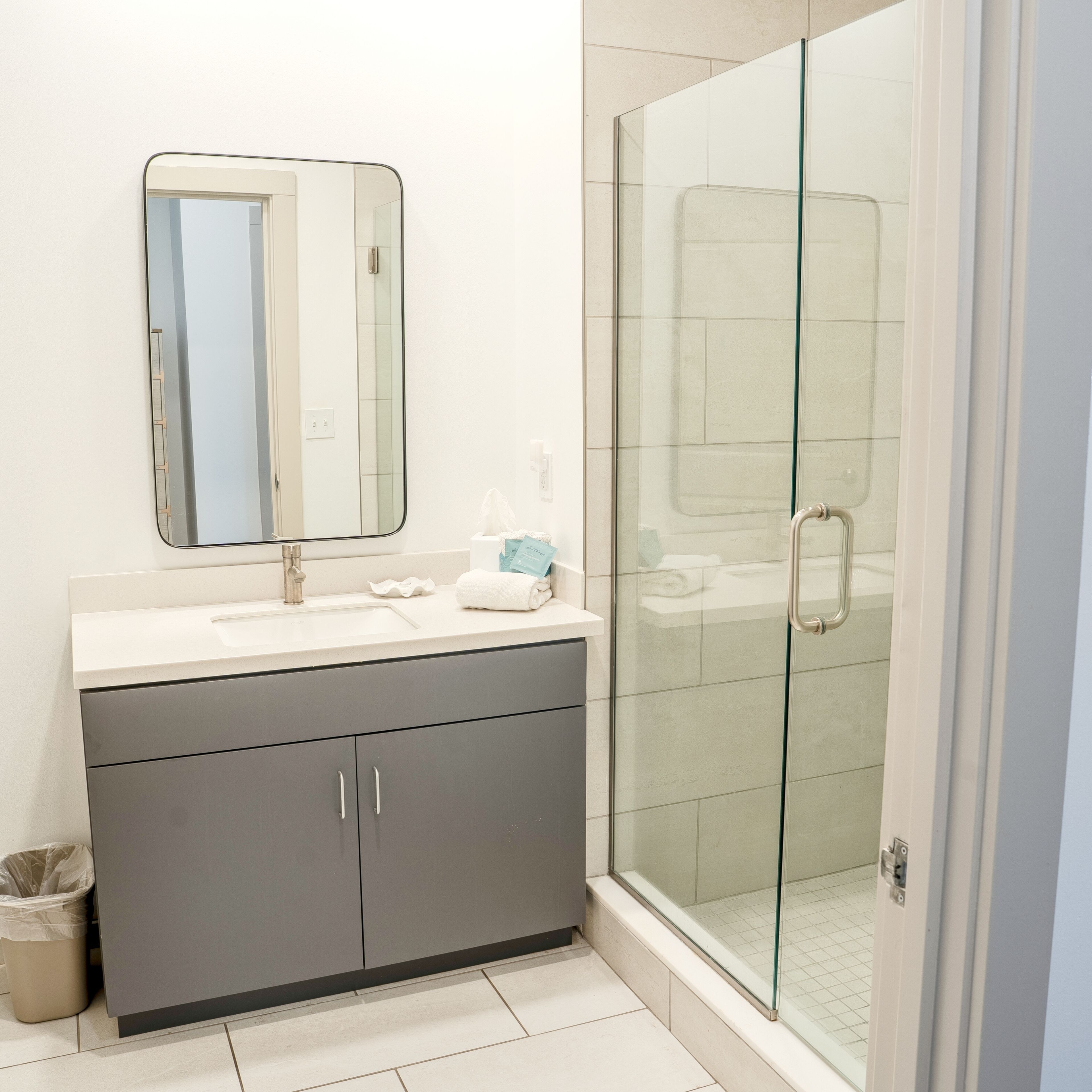 A bathroom with a glass shower enclosure, a sink with a mirror, and a vanity with cabinets.