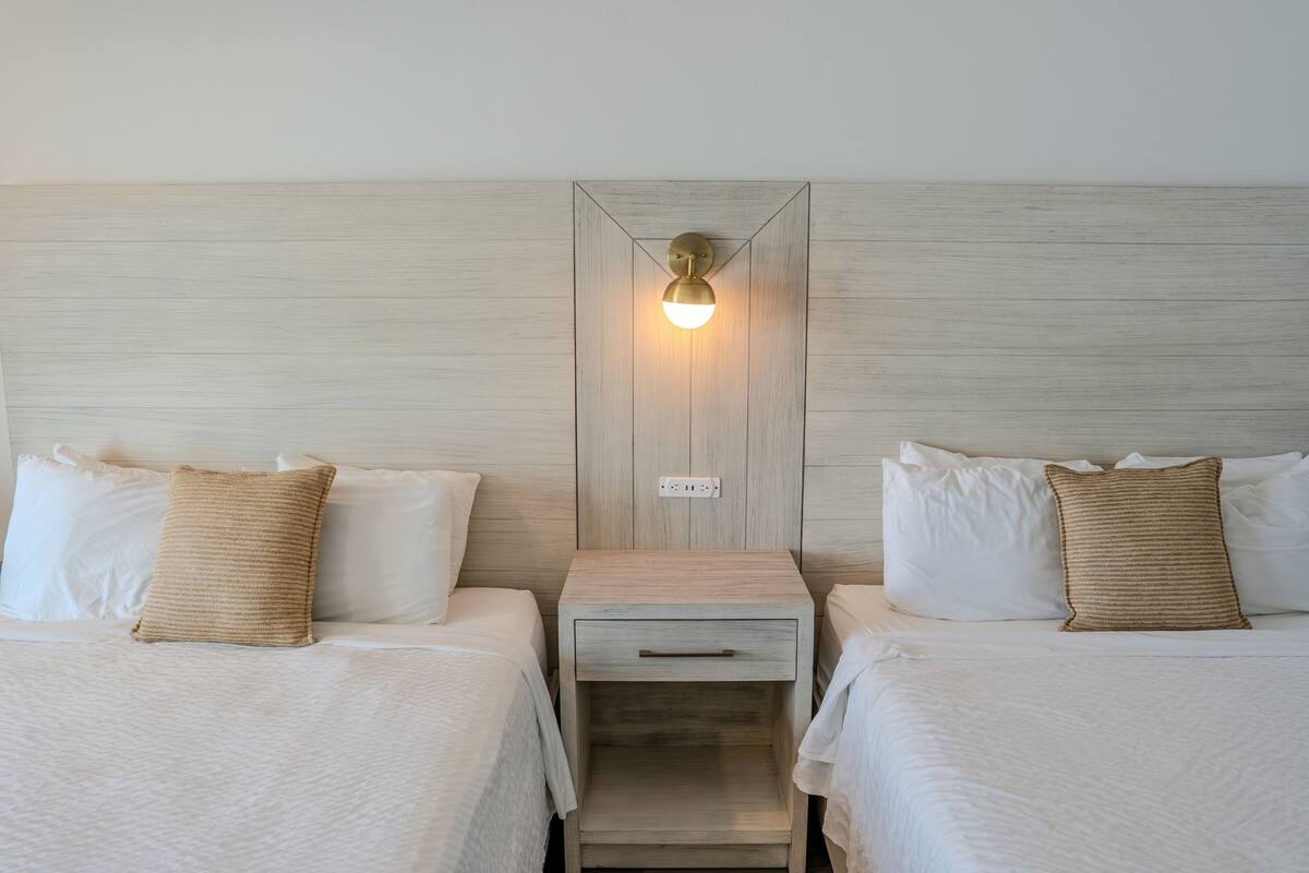 A hotel room with two beds, a nightstand with a lamp, and a wooden headboard.