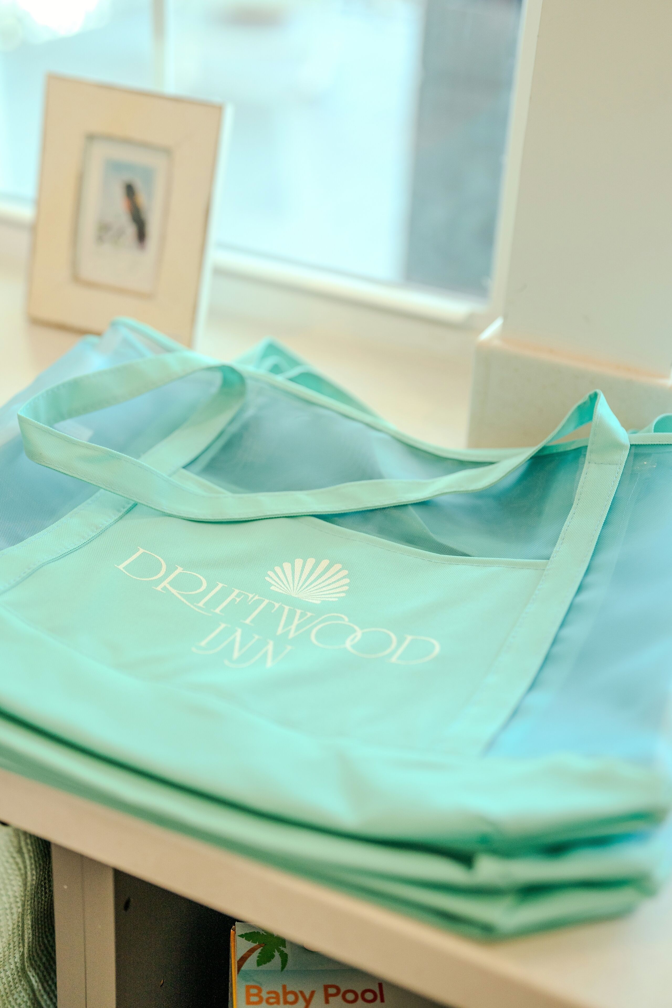 A stack of light blue Drifttwo Inn tote bags on a white surface.