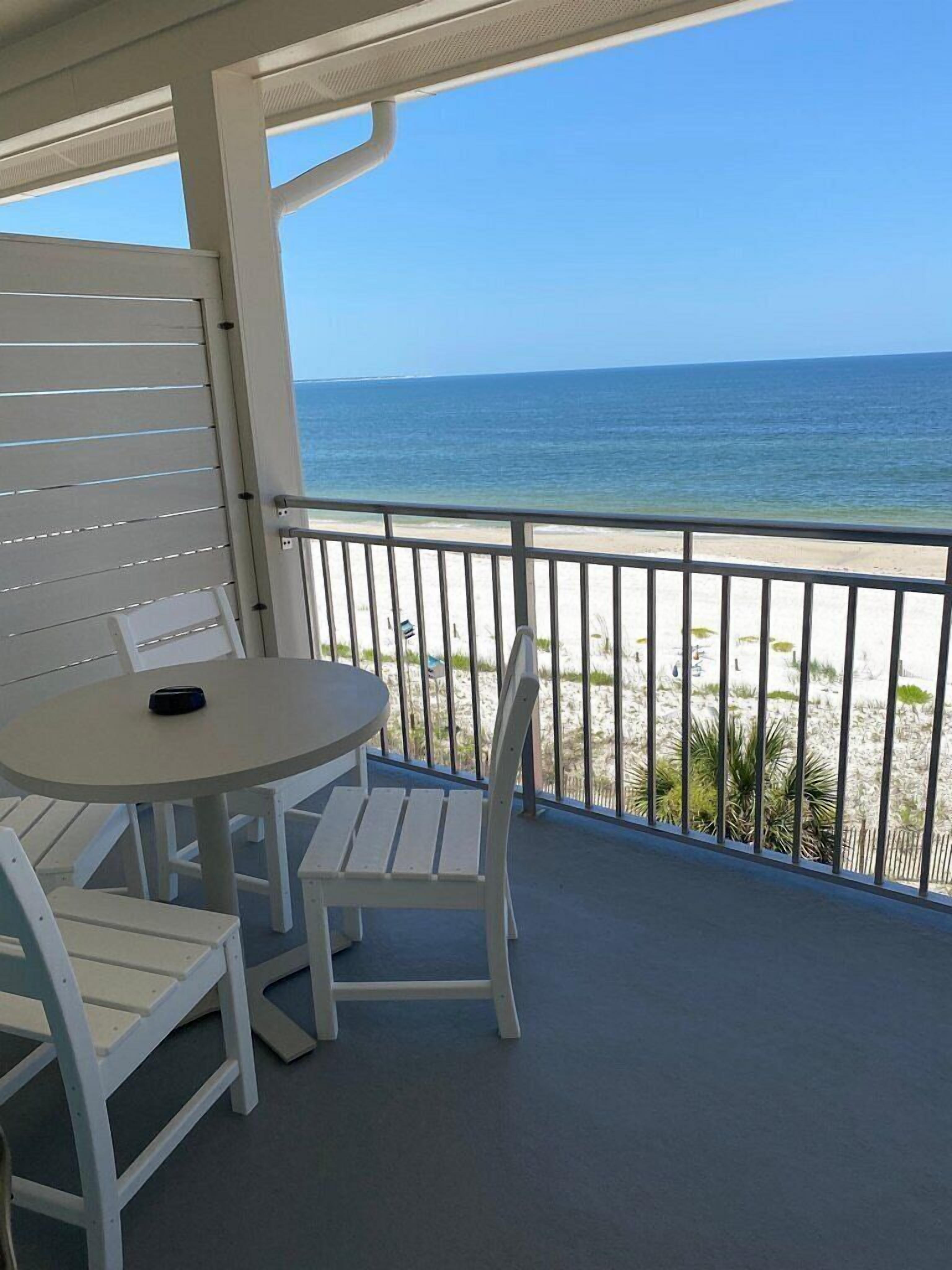 A balcony with a table and chairs, overlooking a beach and ocean.