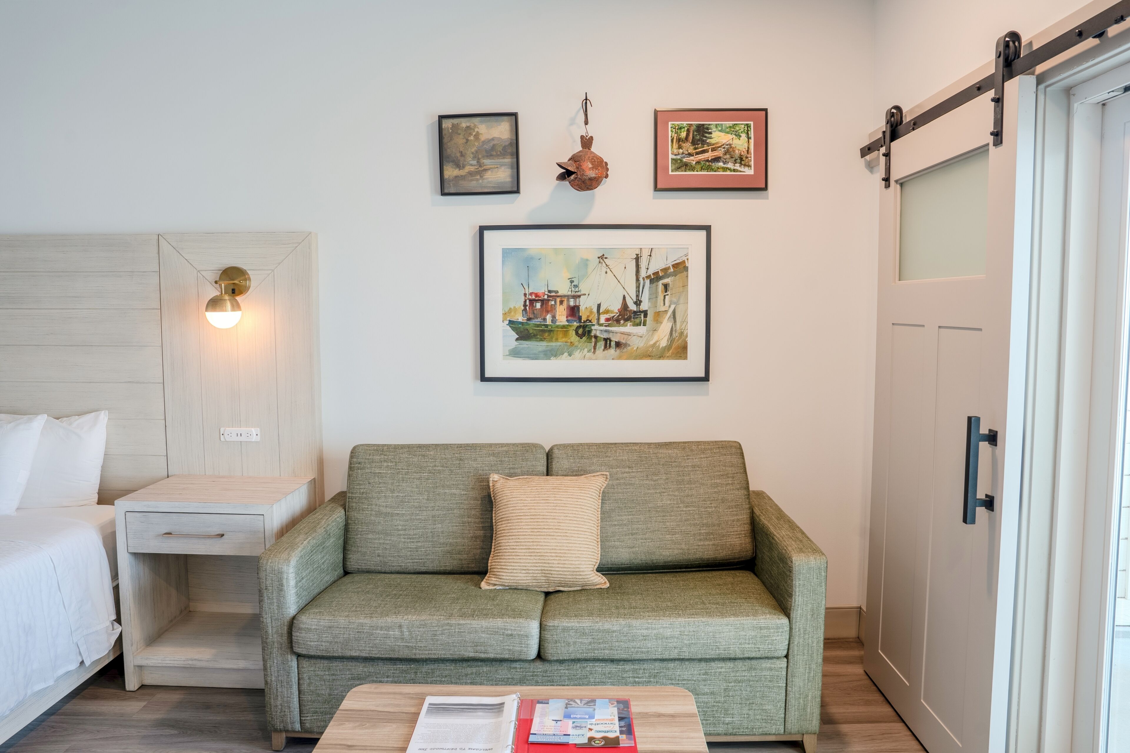 A room with a bed, a wooden nightstand, a green sofa, a coffee table with books, and a painting on the wall.
