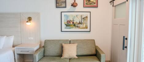 Une pièce comprenant un lit, une table de chevet en bois, un canapé vert, une table basse avec des livres et un tableau accroché au mur.